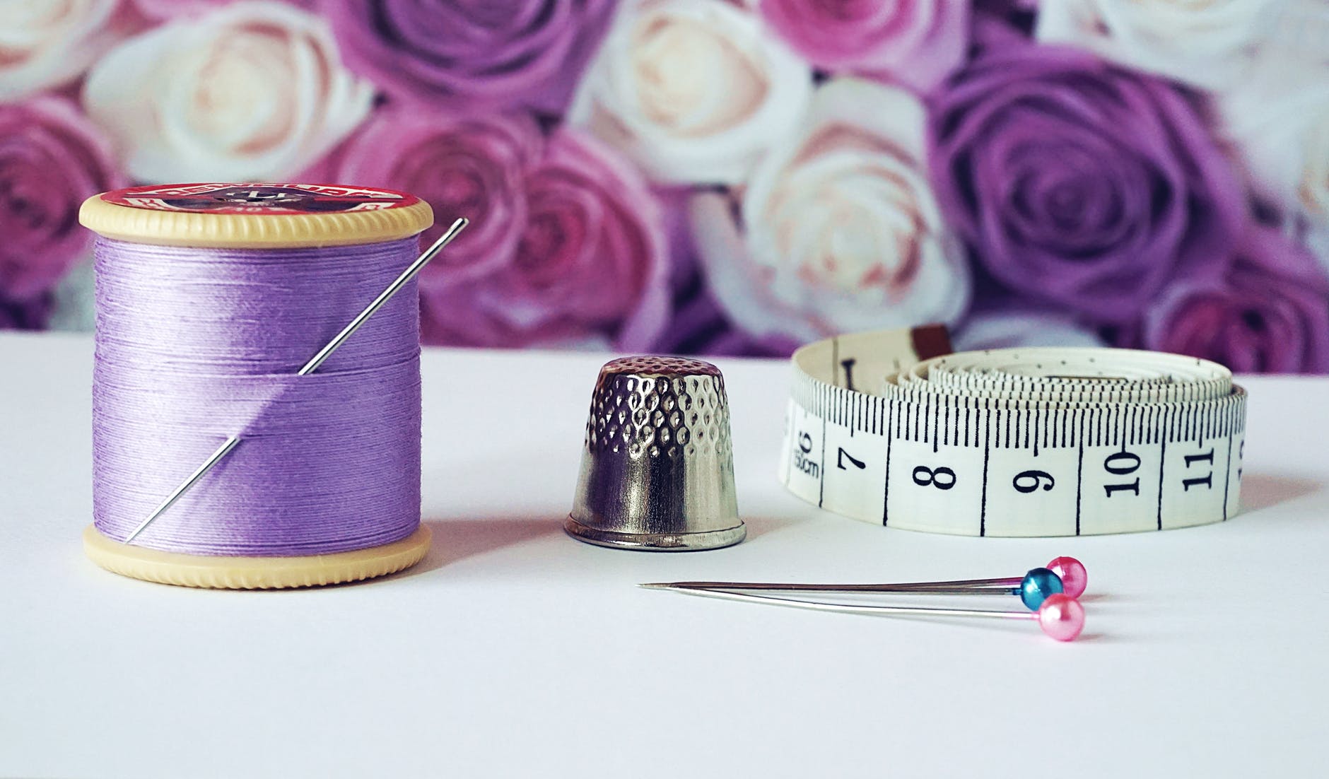 spool of purple thread near needle thimble and measuring tape