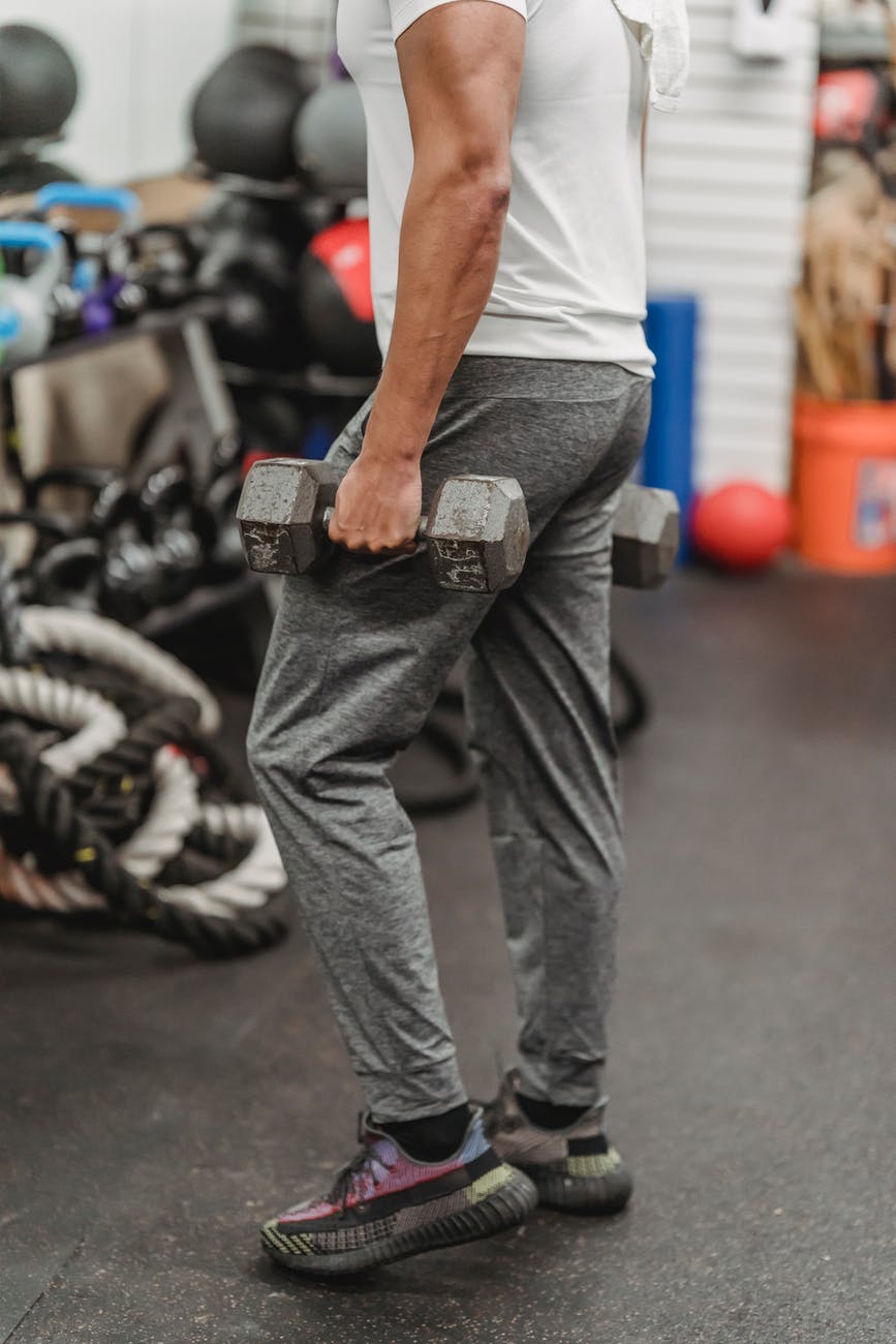 crop sportsman with dumbbell in hand in gym